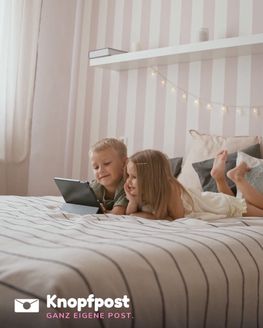Zwei Kinder liegen auf einem Bett und schauen gemeinsam auf ein Tablet
